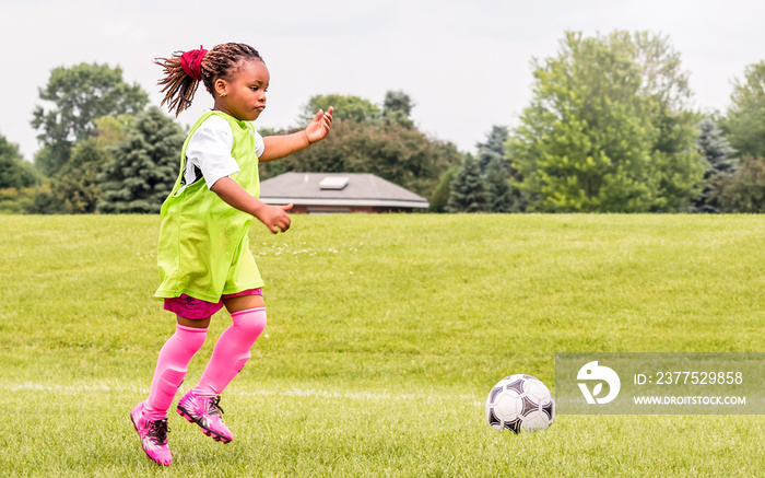 A young African American girl is learning how to play soccer on a sunny day