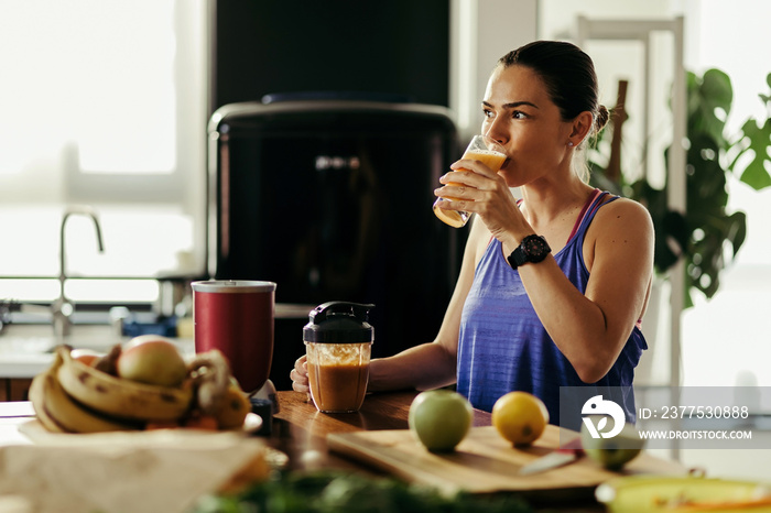 Young athletic woman drinking fruit smoothie in the kitchen.