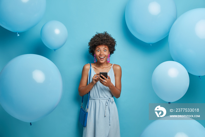 Photo of happy impressed woman being on corporative party, dressed in everything blue, holds smartph