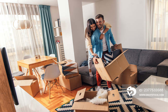 Smiling young couple move into a new home carrying boxes of belongings.