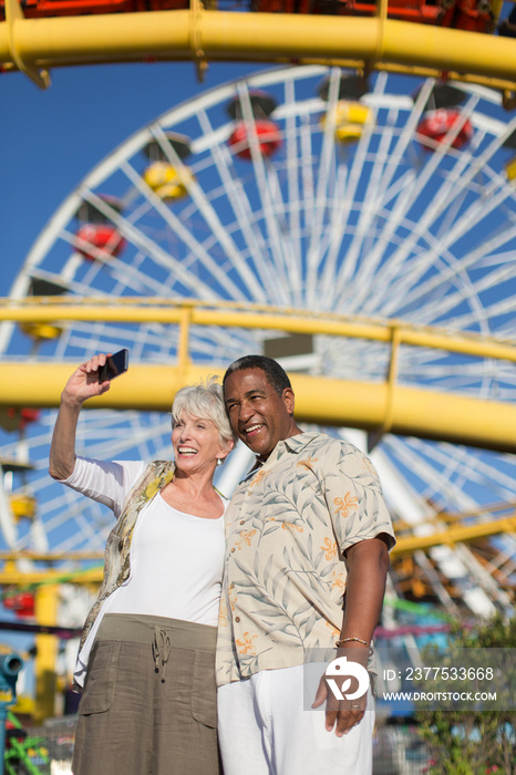 Happy senior couple taking selfie below sunny Ferris Wheel