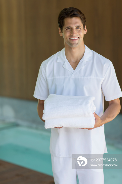 Portrait happy young male masseuse holding towels in spa