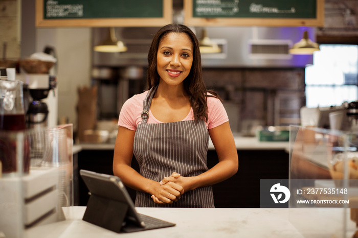 Portrait of smiling female owner with tablet computer on bar counter standing in coffee shop