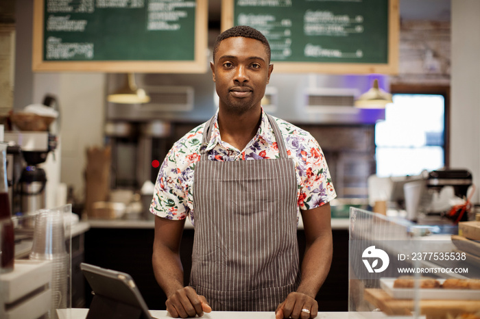 Portrait of confident male barista with tablet computer on bar counter standing in coffee shop