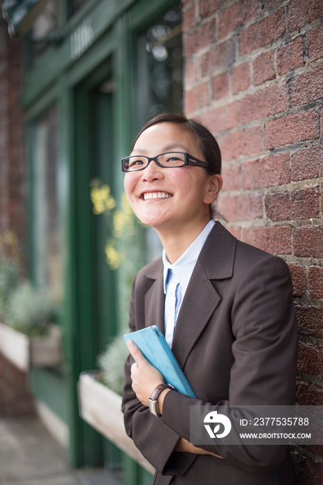 Businesswoman hugging digital tablet next to brick wall