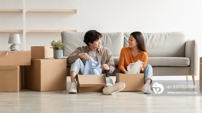 Cheerful Asian couple unpacking belongings and having conversation, moving to new apartment or their