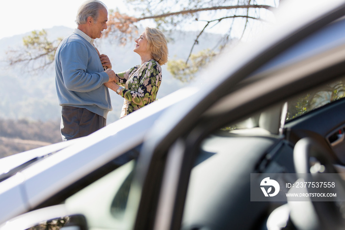 Affectionate senior couple outside car at sunny roadside