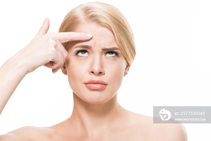 unhappy young woman pointing at wrinkles on forehead and looking up isolated on white