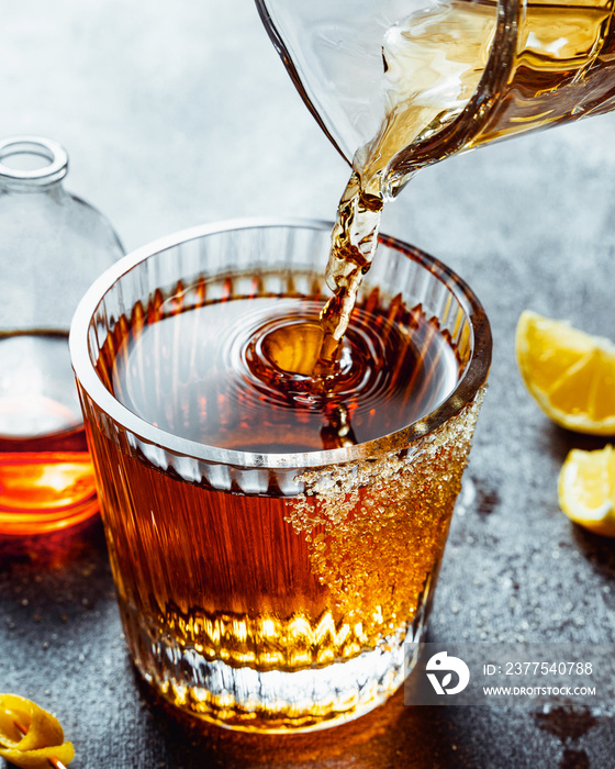 将威士忌倒入装有红糖和柠檬的老式coktail饮料的玻璃杯中。垂直镜头