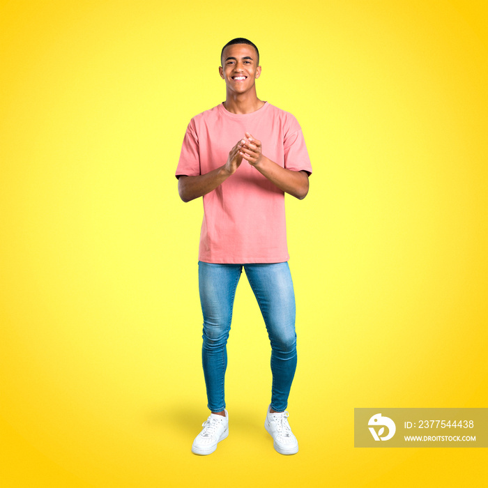 Standing young african american man smiling and applauding on colorful background