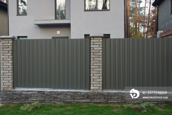 part of the fence of green iron and gray bricks on a rural street