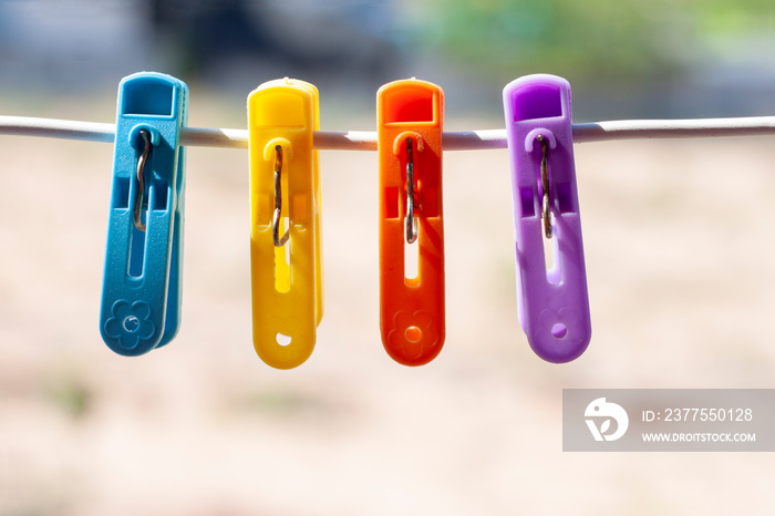 Multi colored plastic clothes clips on the wire on blur nature background.