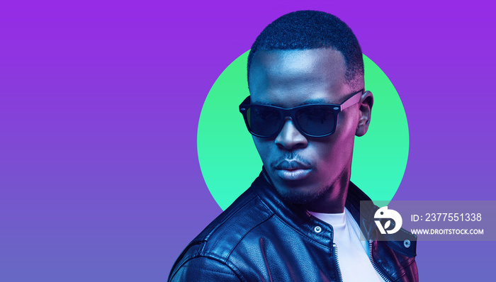 Portrait of stylish african man, wearing leather jacket and sunglasses isolated on purple background