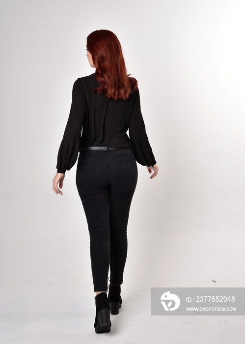 Portrait of a pretty girl with red hair wearing black jeans, boots and a blouse.  full length standi