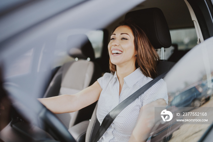 Gorgeous smiling Caucasian brunette driving her car.