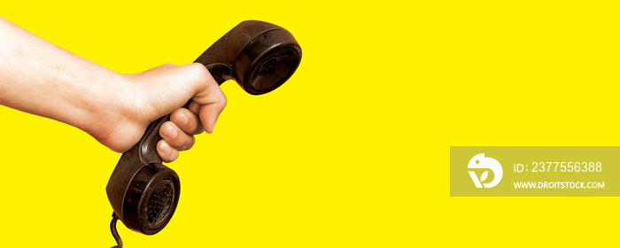 Hand holding old telephone receiver on yellow background.