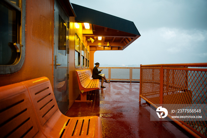 Businesswoman using phone while reading newspaper on ferry at dusk