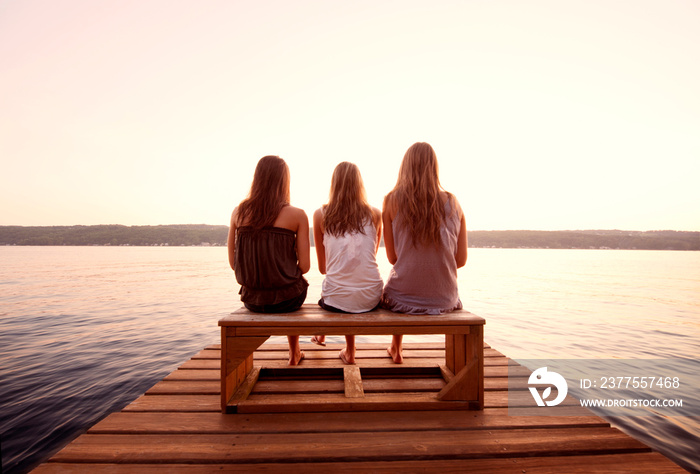 Rear view of three women sitting on pier at lake