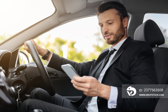 Handsome businessman driving car, using mobile phone