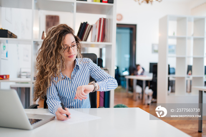 Elegant young woman checking the time on wrist watch at workplace.