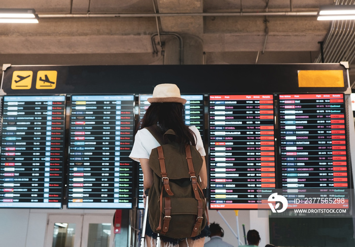 Asian woman traveler looking information board with carrying, suitcase luggage and passenger for tou