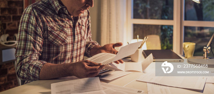 Shocked man checking bills at home