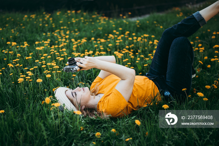 Young beautiful girl in an orange T-shirt holding retro camera in her hands lying on the lawn where 