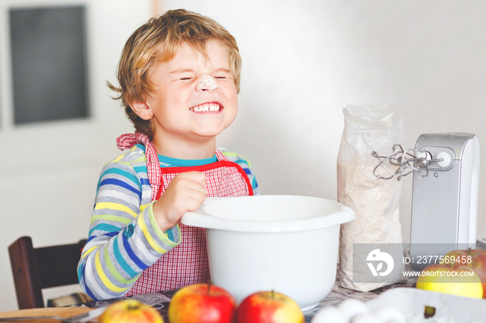 Cute little happy blond preschool kid boy baking apple cake and muffins in domestic kitchen. Funny l