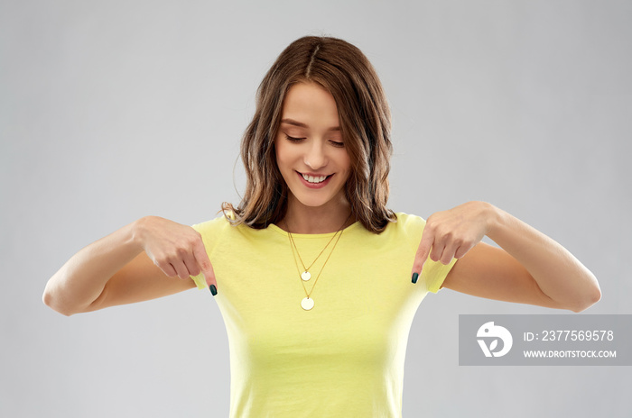 people concept - smiling young woman or teenage girl in blank yellow t-shirt pointing fingers down o