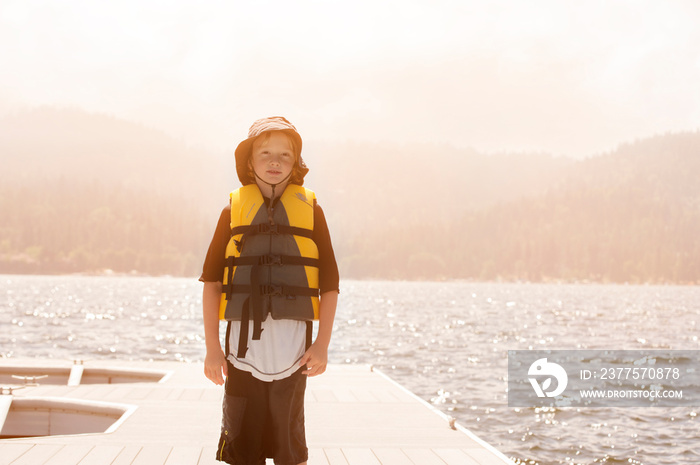 Boy (6-7) Standing On Dock With Life Jacket On