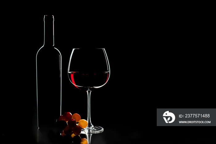 优雅的红酒杯、酒瓶和深色背景上的一串葡萄。