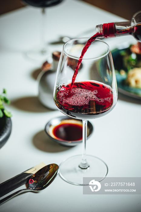 在餐厅的餐桌上，将红酒倒入白桌子上的玻璃杯的选择性焦点镜头