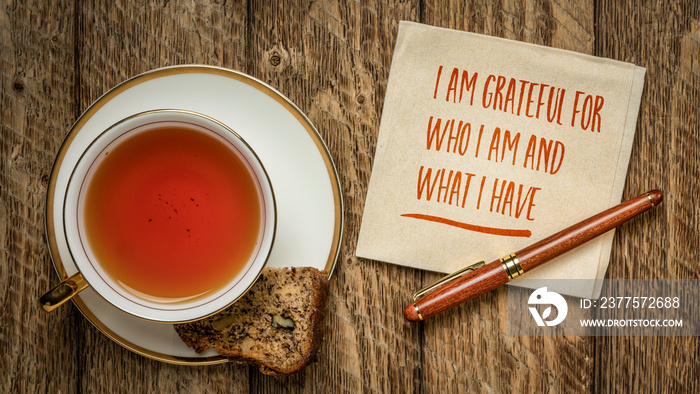 I am grateful for who I am and what I have - inspirational handwriting on a napkin with a cup of tea