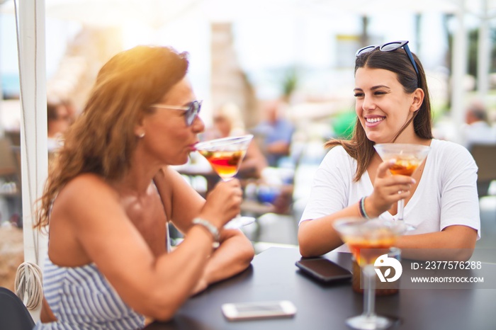 Beautiful mother and daugther sitting at terrace of restaurtant drinking cocktail speaking and smili