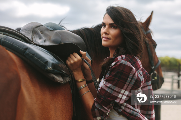 Woman fixing a saddle on her horse