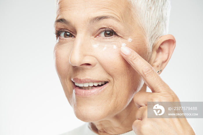 Gorgeous smiling Caucasian senior woman trying out new anti age cream and looking at camera. Beauty 