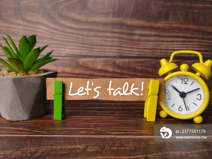 Green plant and alarm clock with text Lets talk!  on a wooden background.