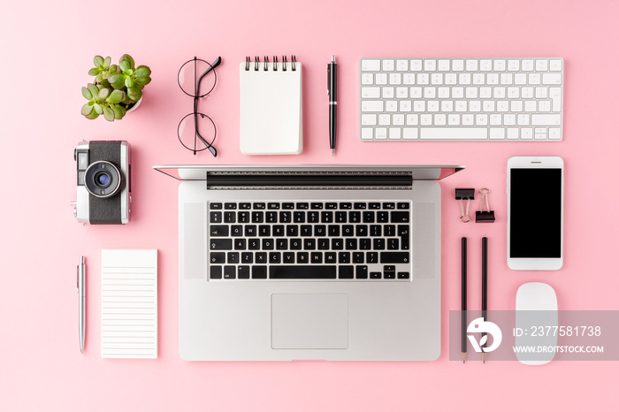 Overhead shot of modern workspace concept with laptop and business accessories on pink background. O