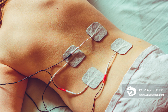 Small white electrodes placed on a woman’s back laying down on a white sheet – Electric device with 