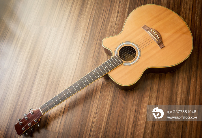 Acoustic guitar laid on wooden floor background. Soft light effect added.