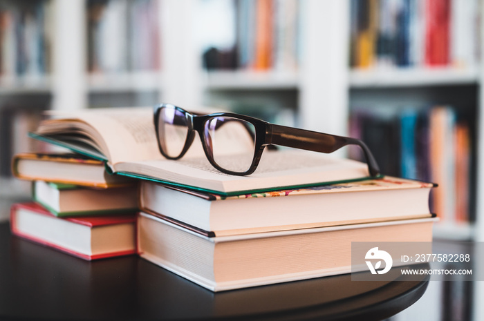 Glasses on stack of books. Library in the background. Books and glasses.