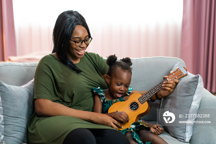 Happy Mom with her daughter playing guitar and singing together at home, happy family