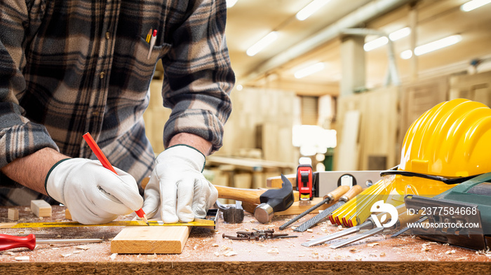 Close-up. Carpenter with his hands protected by gloves with pencil and carpenters square draw the c