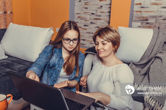 Mother and her teenage daughter relaxing together  watching on line content in a laptop in a living 