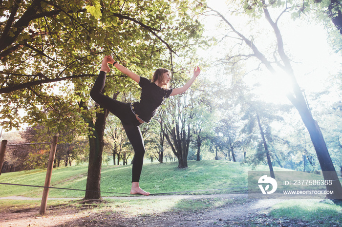 Woman balancing a tightrope or slackline outdoor in a city park in autumn - slacklining, balance, tr