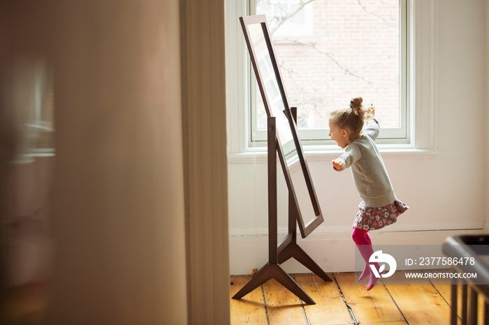 Side view of cheerful girl jumping in front of mirror