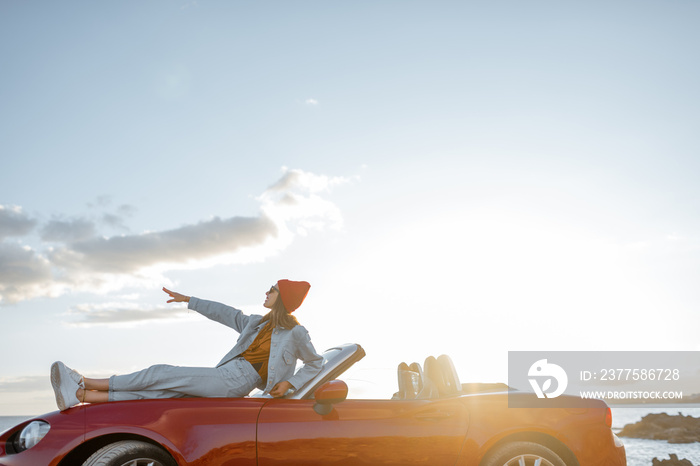 Woman enjoying beautiful landscapes, lying on the car hood while travel on the rocky coastline on a 