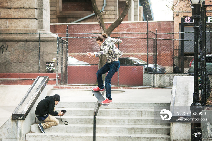 Man photographing friend skateboarding on railing at skateboard park