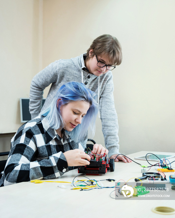 School student making robotic cars. Teenager girl and boy at robotics school makes robot managed fro