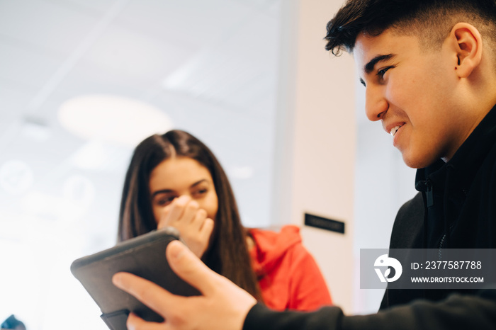 Smiling teenagers using digital tablet while studying in classroom at university